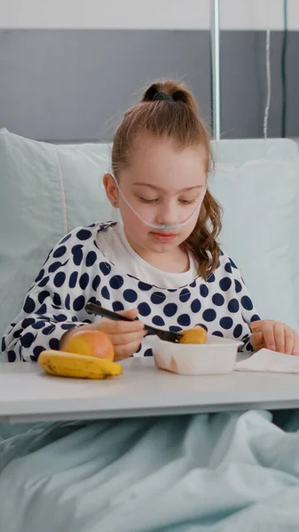 Портрет госпіталізованої маленької дитини, що відпочиває в ліжку, їсть здорову їжу під час огляду відновлення — стокове фото