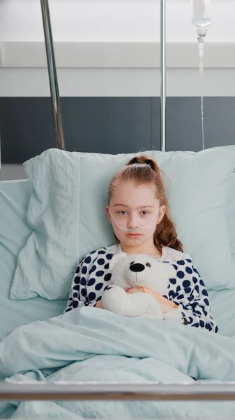 Retrato de paciente hospitalizado menina doente criança segurando ursinho descansando na cama durante a consulta médica — Fotografia de Stock