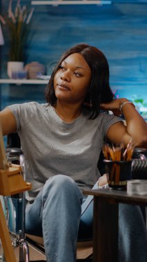 Tekerlekli sandalyede oturan kötürüm siyahi sanatçı tuvale resim çiziyor.