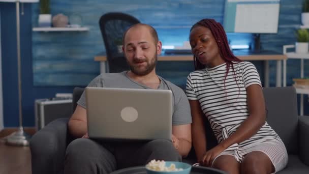 Modern interracial couple using laptop on couch at home — Stock Video