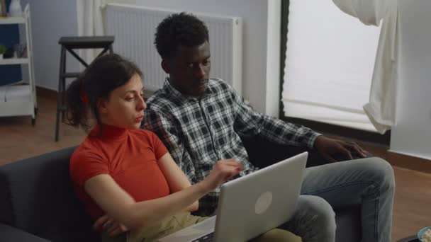 Interraciale paar zitten op de bank met behulp van laptop in de woonkamer — Stockvideo