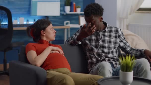Międzyrasowa para spodziewa się dziecka w salonie — Wideo stockowe