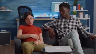 Hamileliği olan ırklar arası bir çift evdeki kanepede dinleniyor.