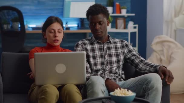 Mezirasový pár se dívá na notebook a sedí na pohovce — Stock video