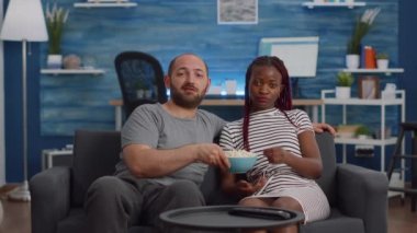 Oturma odasında televizyon izleyen ırklar arası genç çift.