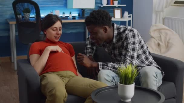 Mladý mezirasový pár očekává dítě sedí na pohovce — Stock video