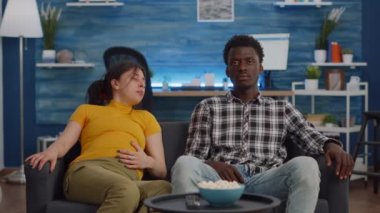 Oturma odasındaki koltukta oturan ırklar arası hamile bir çift.