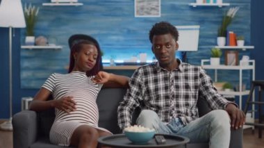 Hamileliği olan siyahi çift evde televizyon seyrediyor.