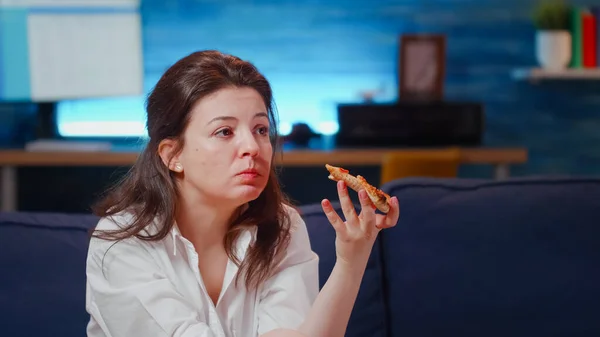 Joven comiendo rebanada de pizza mientras ve la televisión — Foto de Stock