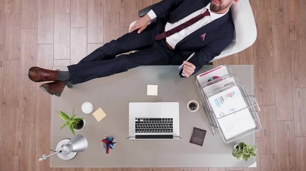 Вид сверху бизнесмена в костюме, расслабленного ногами на рабочем столе — стоковое фото