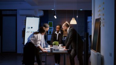 Çeşitli çok ırklı iş adamları konferans masasında duran grafikler üzerinde tartışıyor.