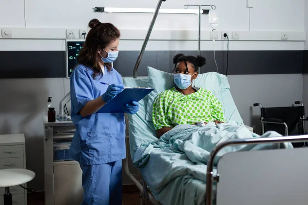 Caucasian nurse checking on sick african american patient — Stock Photo, Image