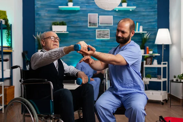 Medico professionista che aiuta il pensionato anziano sulla sedia a rotelle a fare esercizio di forza fisioterapia — Foto Stock