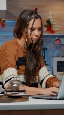 Beyaz kadın kışın dekore edilmiş mutfakta dizüstü bilgisayar kullanıyor.