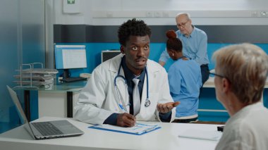 Afrikalı Amerikalı doktor yaşlı bir kadına danışıyor.