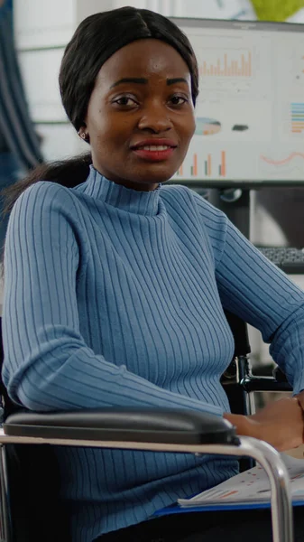 Africano mulher empregado olhando para câmera sorrindo sentado em cadeira de rodas — Fotografia de Stock