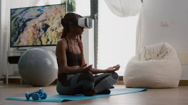 Чорна навчальна жінка в гарнітурі віртуальної реальності сидить на карті йоги Стокова Картинка