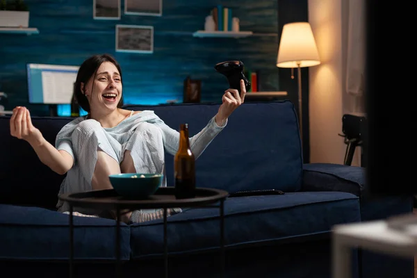 Жінка-гравець грає у відеоігри з джойстиком, сидячи на дивані у вітальні — стокове фото