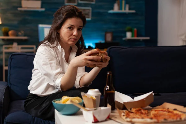 Portret van een ontspannen vrouw op zoek naar camera met lekkere hamburger in handen tijdens fastfood nacht — Stockfoto