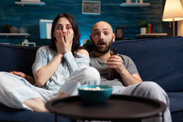Zmatený šokovaný pár sledující televizní film v noci a jíst popcorn, — Stock fotografie