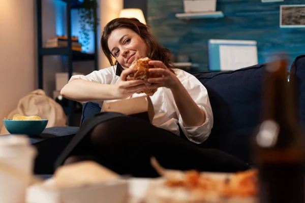 Vrouw praten aan de telefoon met vrienden terwijl het houden van lekkere heerlijke hamburger in handen ontspannen op de bank — Stockfoto
