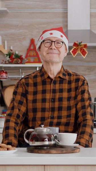 Portrait of senior man wearing santa hat smiling while looking into camera during christmas morning — Stock Photo, Image