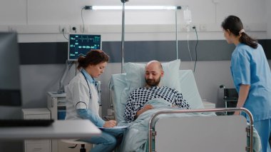 Siyahi hemşire hastanın hayati değerlerini kontrol ediyor. Kalp atış hızını kontrol ediyor.