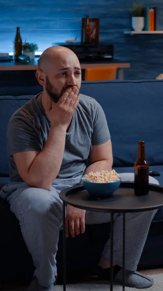 Homem focado olhando para o filme de drama, chorando sentado no sofá comendo pipocas — Fotografia de Stock