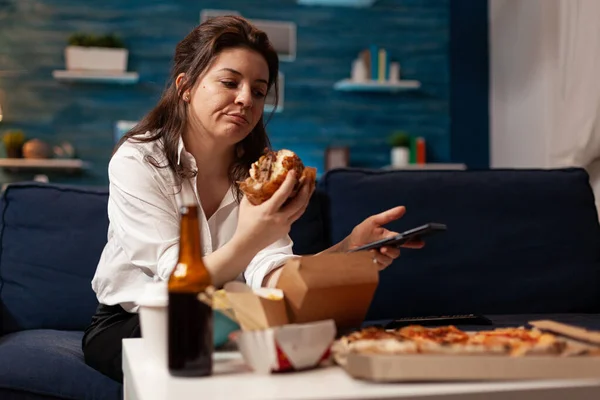 Blanke vrouw met smaak burgery in handen browsen op sociale media met behulp van smartphone — Stockfoto