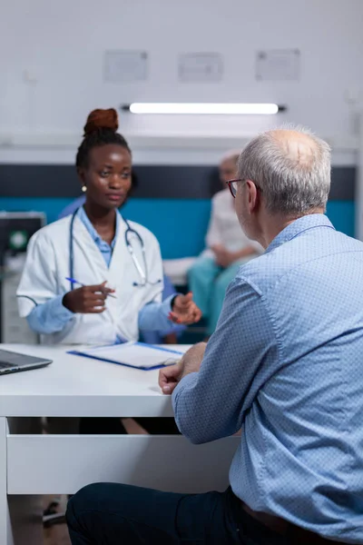 Afrykański amerykański lekarz omawiający wyniki badań ze starym pacjentem — Zdjęcie stockowe