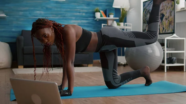 Mujer negra adulta sentada en el mapa de yoga viendo entrenamiento de fitness en línea — Foto de Stock