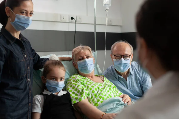 Family wearing protective face mask against coronavirus while visiting elderly senior woman — Stock Photo, Image