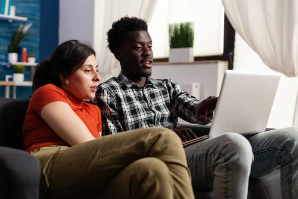 Casal interracial olhando para o computador portátil moderno — Fotografia de Stock