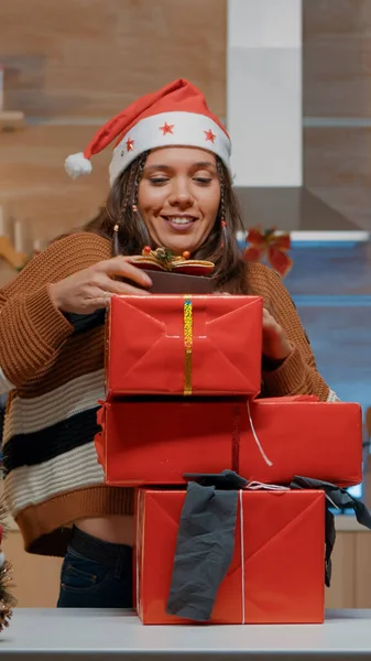 Žena se Santa kloboukem nesoucí dárky v zdobené kuchyni — Stock fotografie