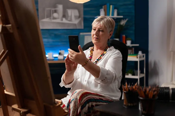 Artista senior usando smartphone sentado en la sala de estudio de arte — Foto de Stock