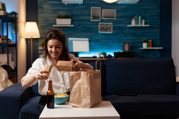 Lachende vrolijke vrouw uitpakken proeven fast-food huis geleverd zittend op de bank — Stockfoto