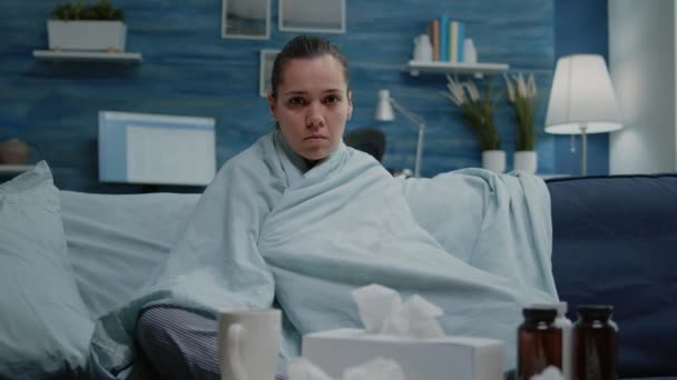 Frau mit Virusinfektion sitzt in Decke und blickt in Kamera — Stockvideo