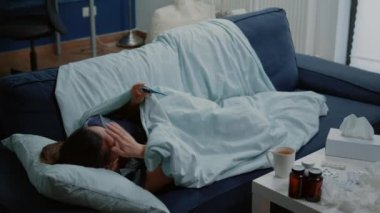 Kanepede yatıp ateşini ölçen hastalıklı kadın.