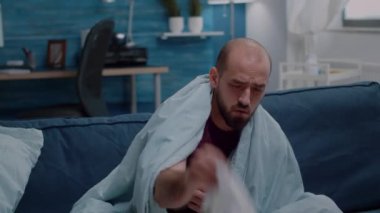 Başı ağrıyan, burnu peçeteyle akan hasta bir adam.