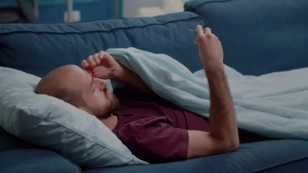 Kranker Mann schaut auf Thermometer, um Fiebermessung zu überprüfen — Stockvideo