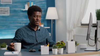 Afrika kökenli Amerikalı yönetici evden çalışıyor, kahveyi yudumluyor ve bilgisayarda daktilo yazıyor.