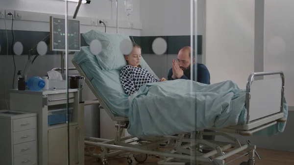 In hospital ward sick girl patient sleeping while worried father praying for sickness recovery — Stock Photo, Image