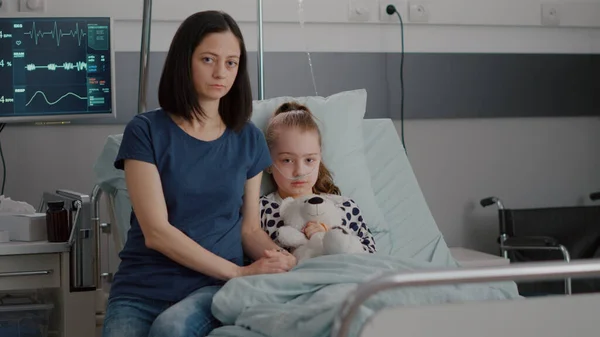 Porträtt av orolig mor sitter bredvid sjukhus lilla barn tittar in i kameran — Stockfoto