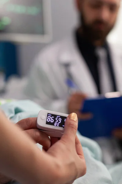 アシスタント看護師を指に医療用酸素濃度計を置く一方、医師の男は心拍数を書き込みます — ストック写真