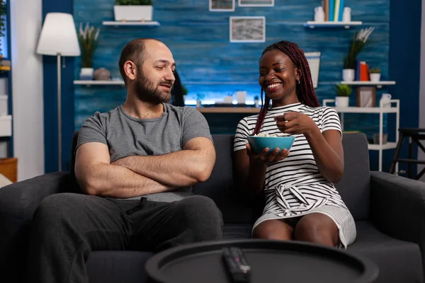 Casal interracial casal rindo e conversando na sala de estar — Fotografia de Stock