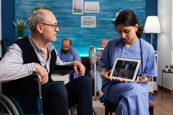 Assistente sociale infermiere che spiega radiografia medica utilizzando tablet computer al pensionato — Foto Stock