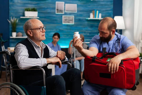 Assistere infermiere spiegando pillole trattamento per l'uomo anziano — Foto Stock