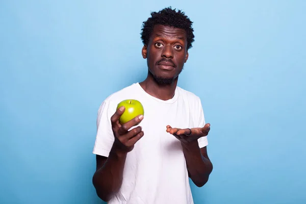 Jeune adulte montrant pomme verte à la caméra en studio — Photo