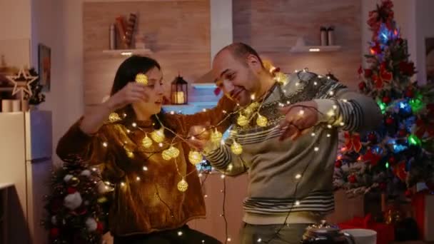 Cheerful couple getting tangled in string of twinkle lights — Stock Video
