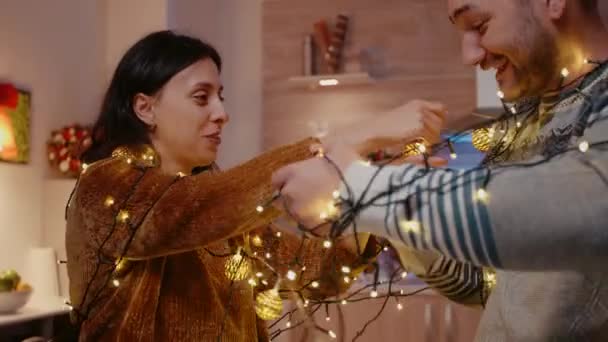 Couple laughing and getting tangled in string of christmas lights — Stock Video